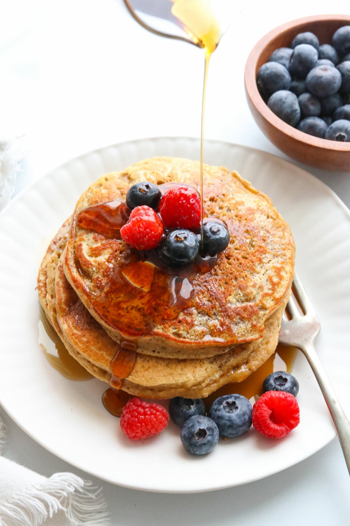protein pancakes topped with berries and maple syrup drizzled on top.