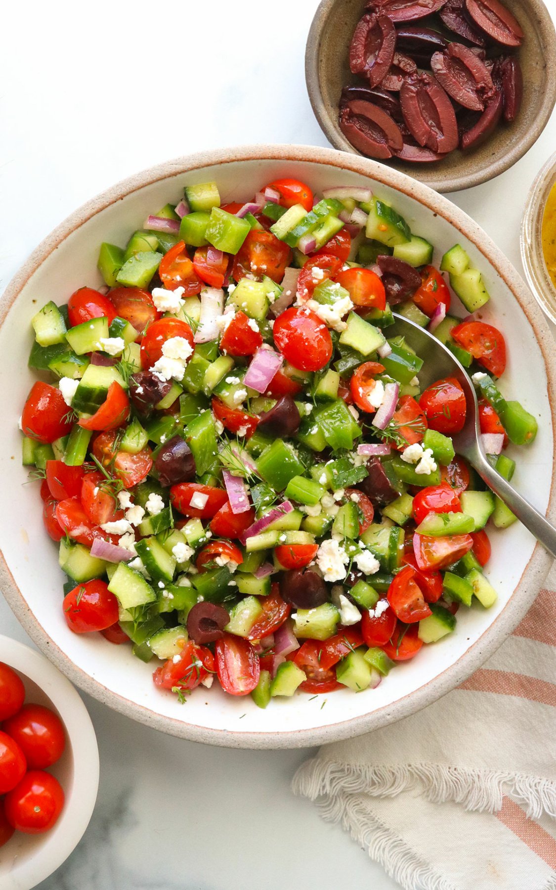 Greek salad topped with feta cheese and stirred with a spoon.