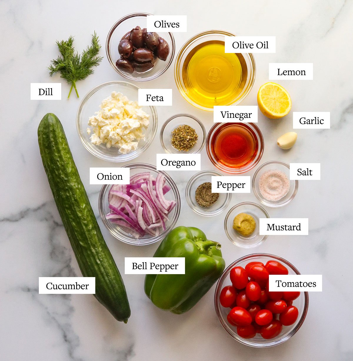Greek salad ingredients labeled on a marble surface.