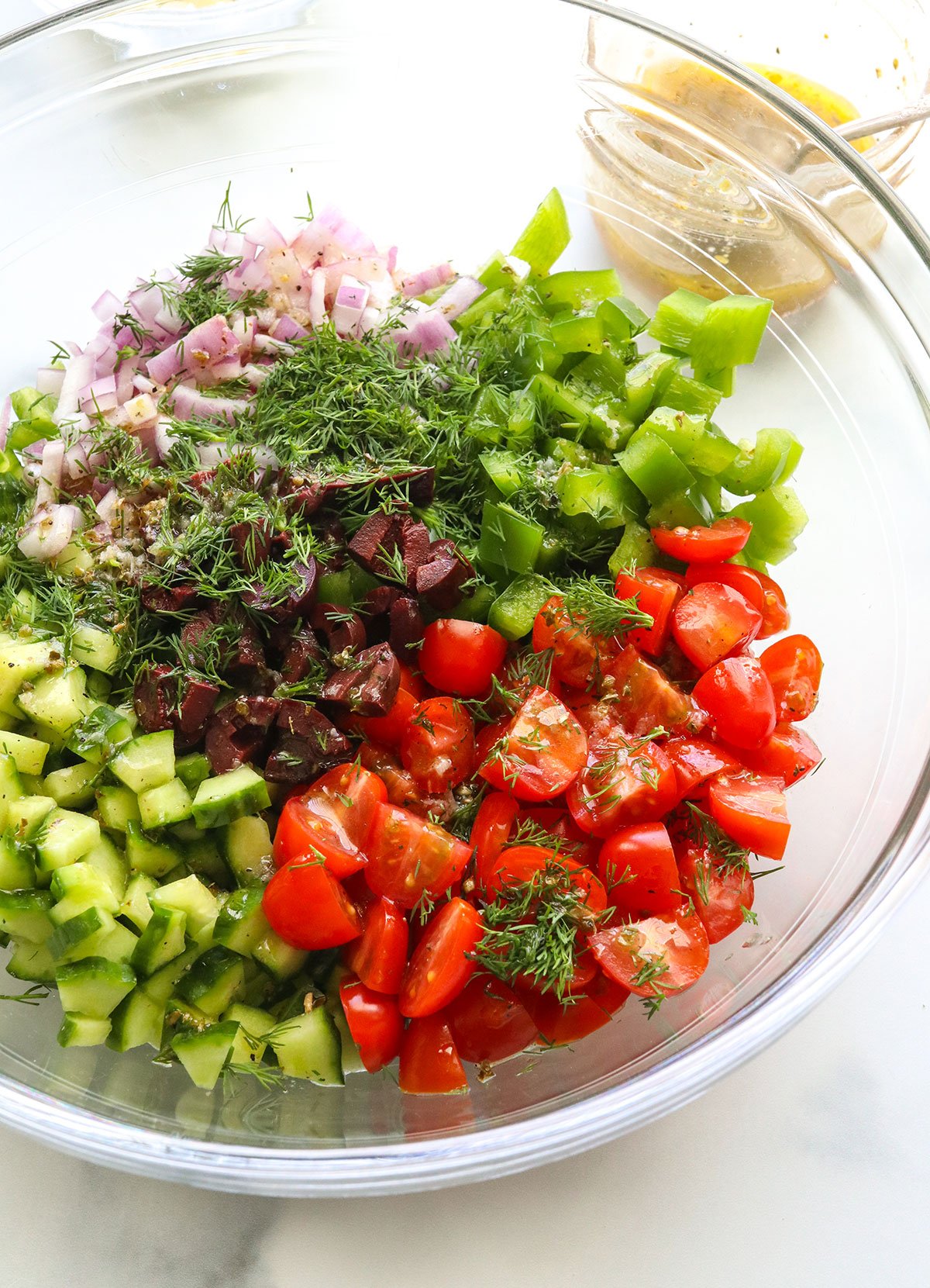 tomatoes cucumber dill and bell pepper tossed with dressing in a large bowl.