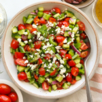 feta and fresh dill sprinkled on a Greek salad in a white bowl.