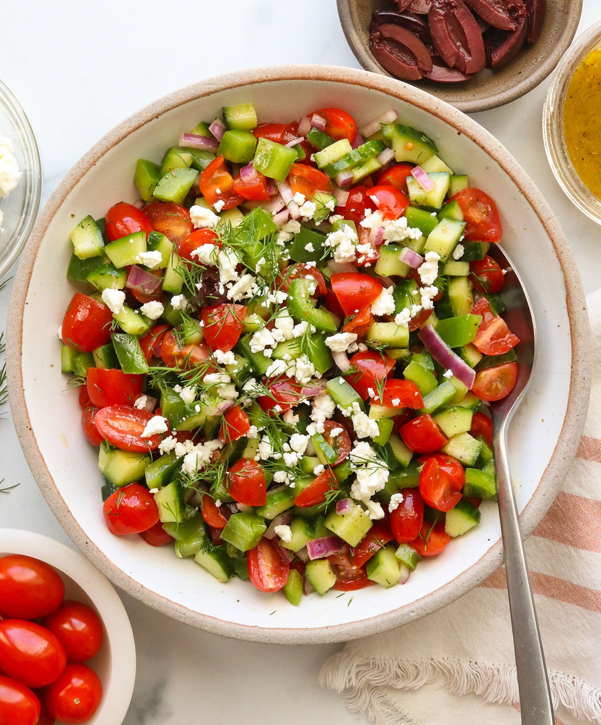 feta and fresh dill sprinkled on a Greek salad in a white bowl.