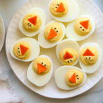 easter deviled eggs served on a white plate with carrot beaks.