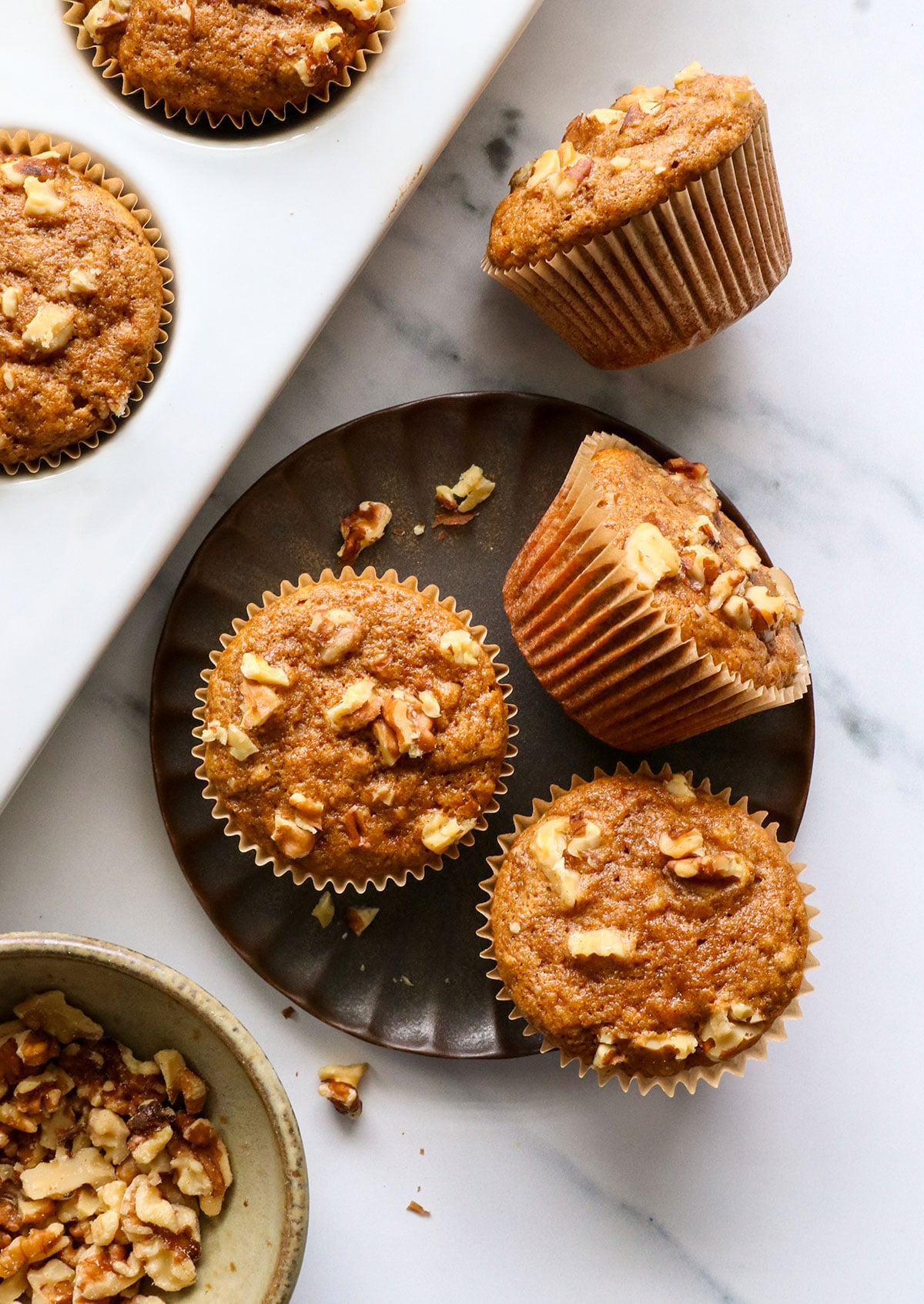 healthy banana muffins on a dark plate with walnuts on top. 