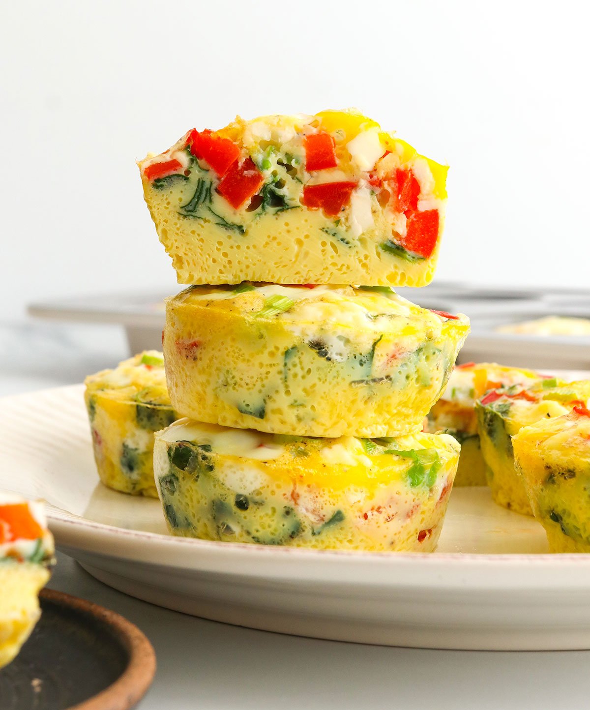 egg muffins stacked on a white plate with the top one sliced in half.