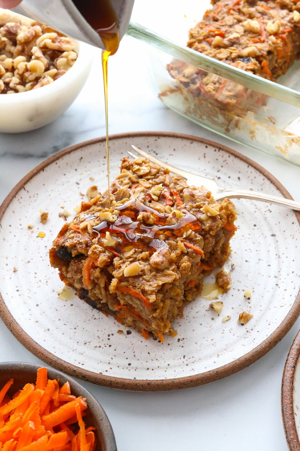 carrot cake oatmeal slice on a plate drizzled with maple syrup.