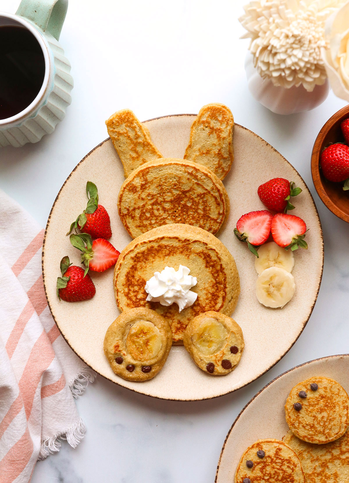 bunny pancakes assembled on a plate with whipped cream tail. 