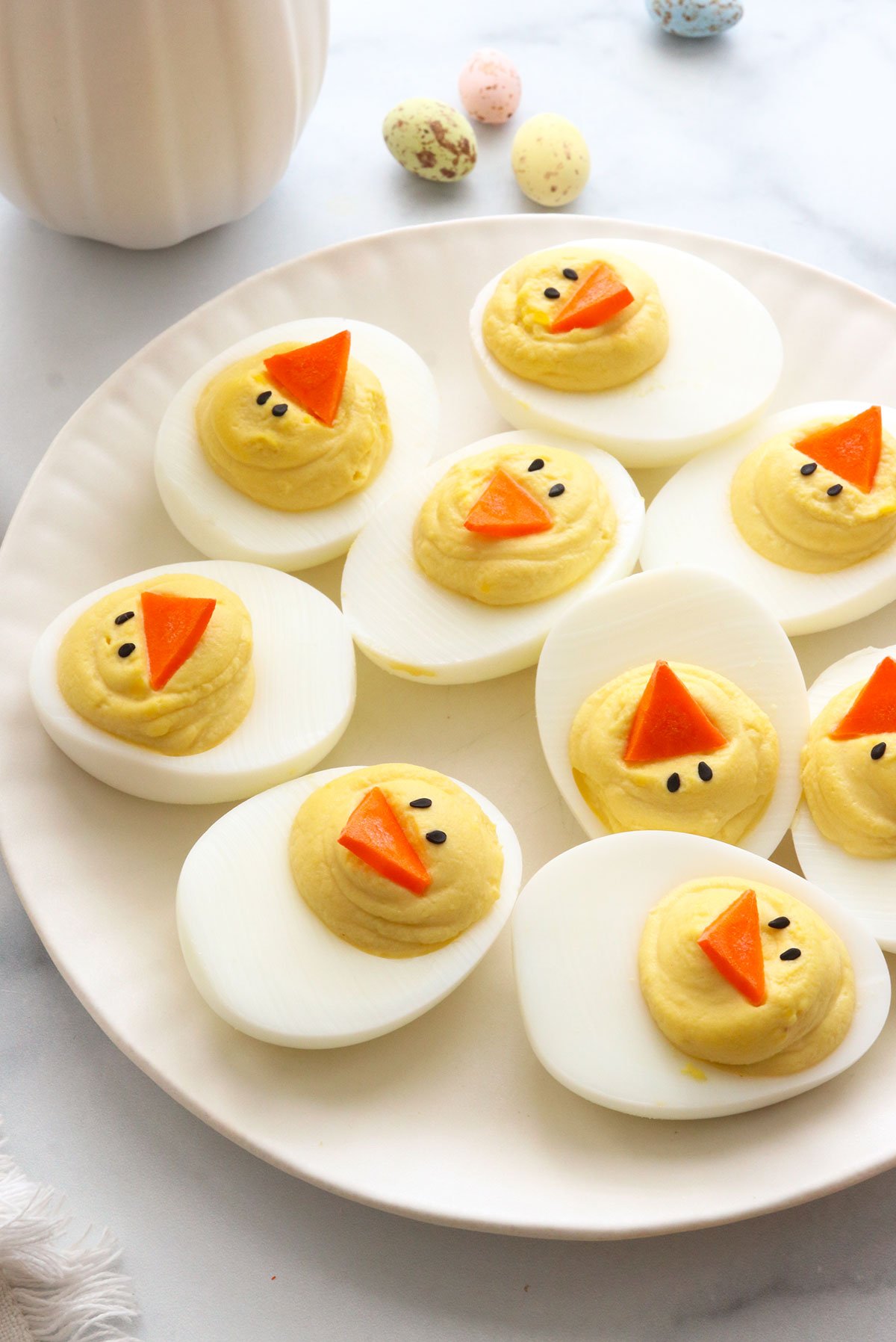 Easter deviled eggs topped with carrot beaks on a white plate.