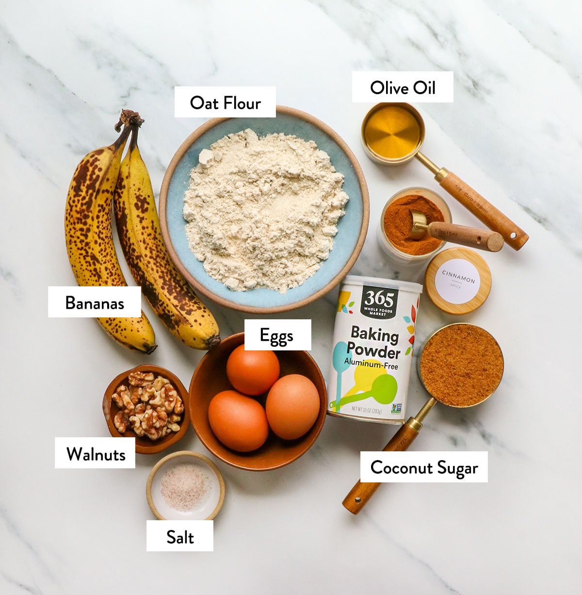 oat flour, bananas, eggs, olive oil, walnuts, coconut sugar, and spices labeled in bowls. 