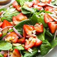 spinach strawberry salad tossed with balsamic dressing on an oval plate.