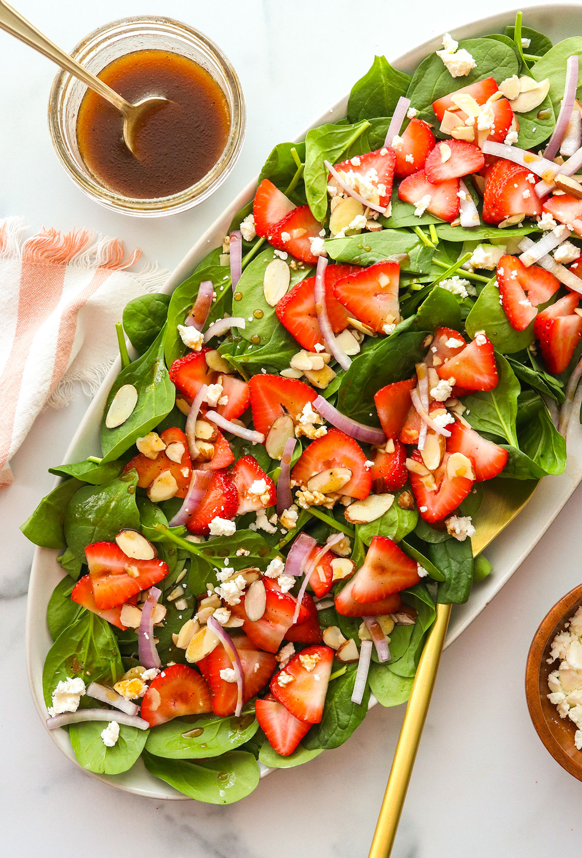 spinach strawberry salad served on an oval plate with dressing on the side.