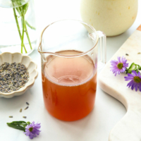honey lavender syrup in a glass jar near purple flowers.