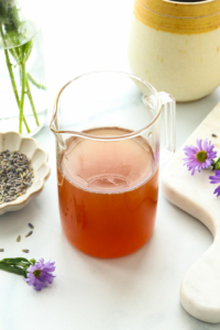 honey lavender syrup in a glass jar near purple flowers.