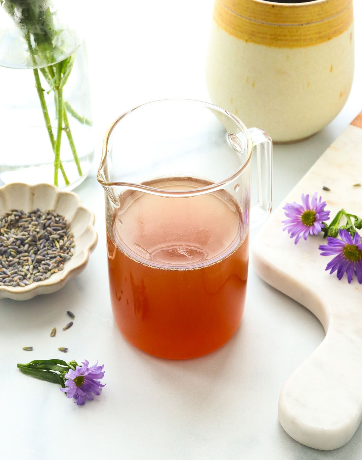 honey lavender syrup in a glass jar near purple flowers. 