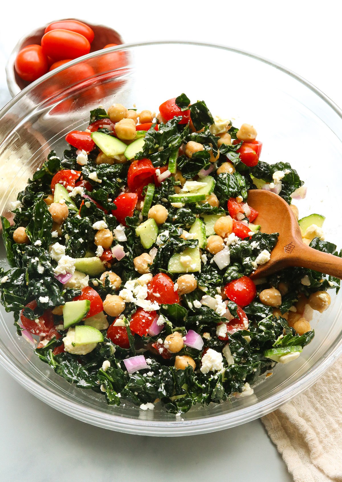 kale and feta salad tossed with tomatoes and cucumber with a wooden spoon.