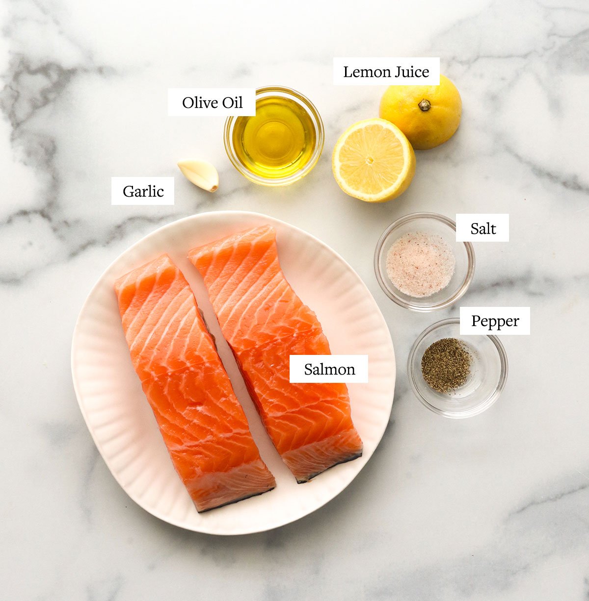 salmon fillets on a white plate with a sliced lemon, garlic, olive oil, salt and pepper.