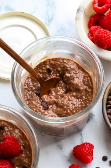 chocolate chia pudding in two glass jars with raspberries.