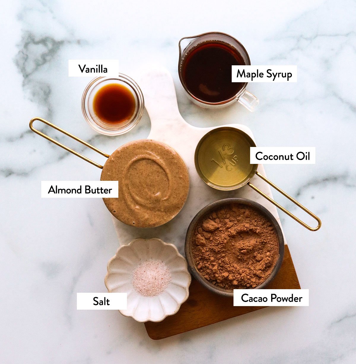almond butter, cacao powder, vanilla extract, maple syrup, and salt labeled in bowls. 