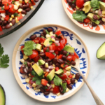 black bean salad served on two colorful plates and topped with avocado chunks.