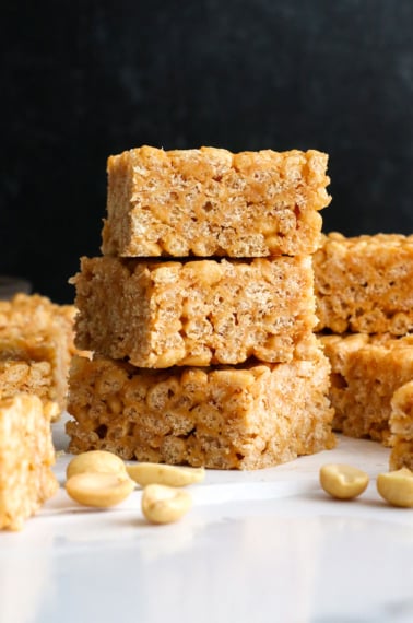 peanut butter rice crispy treats stacked in front of a black background.