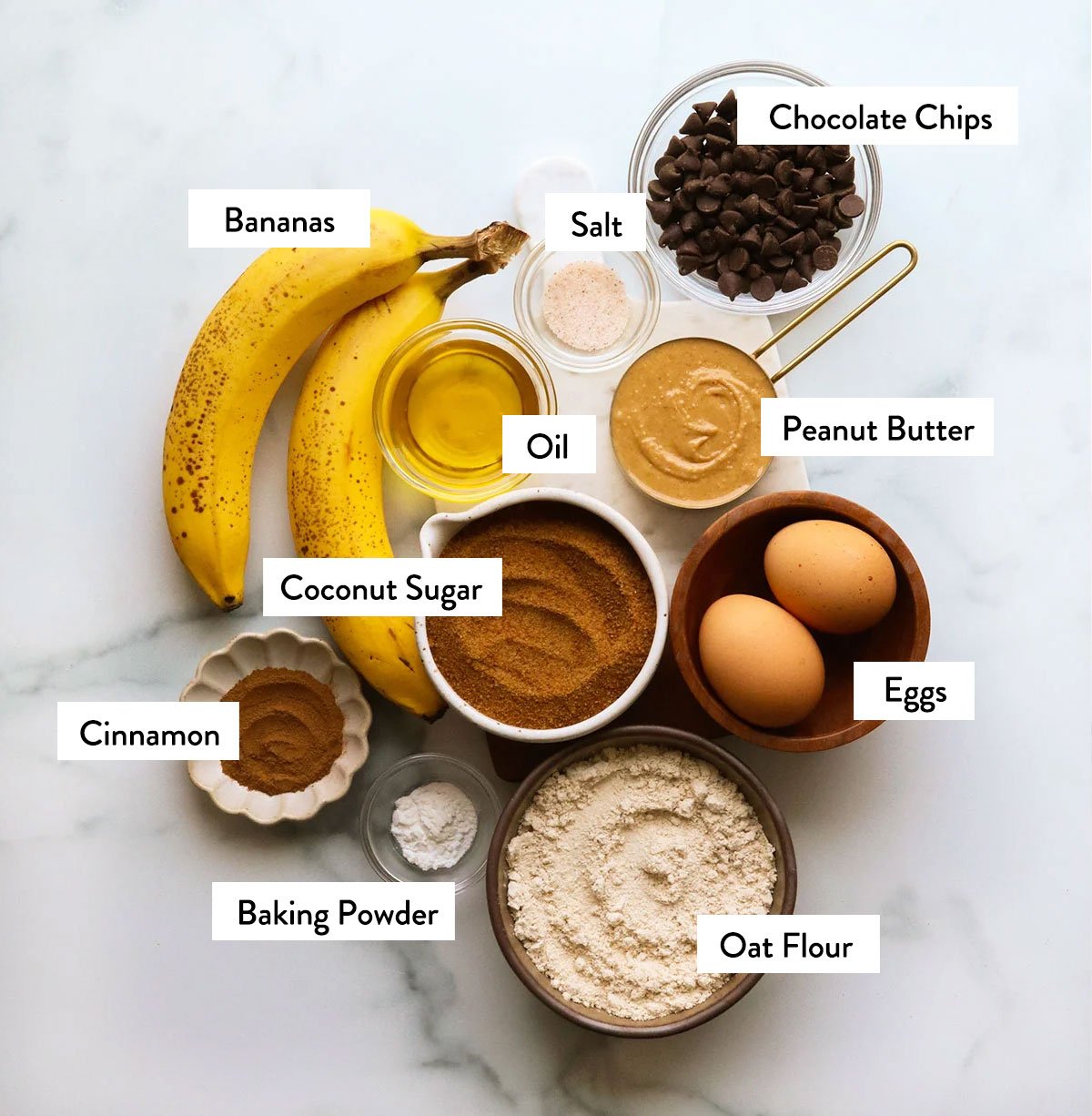oat flour, bananas, coconut sugar, chocolate chips, and eggs labeled in bowls.