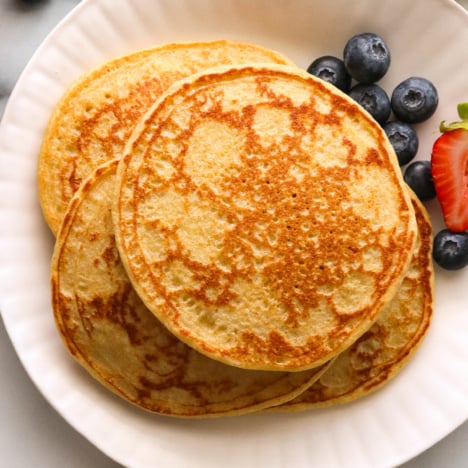 cottage cheese pancakes stacked on a white plate with berries.