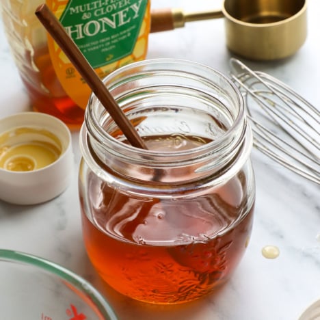 honey simple syrup recipe in a glass jar with a spoon.