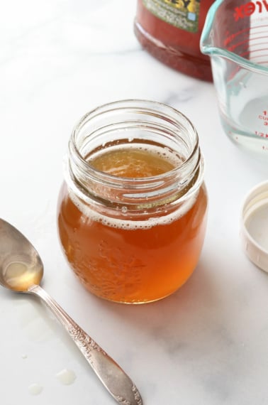 honey simple syrup in a glass jar near a spoon.