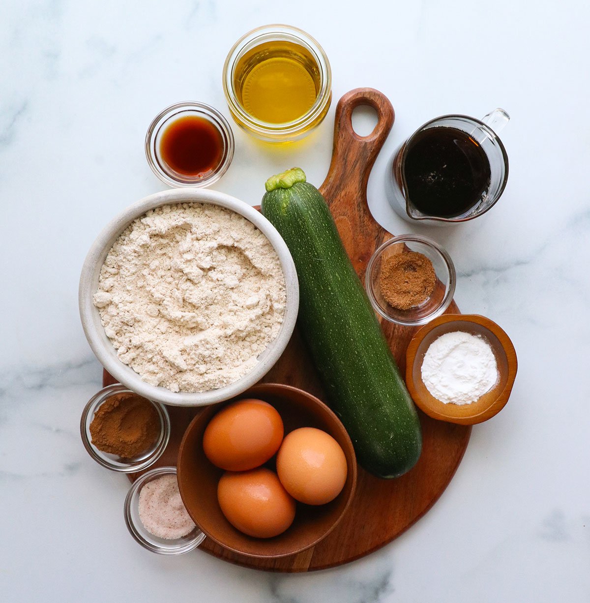 zucchini, eggs, oat flour, baking powder, oil, and maple syrup arranged on a board overhead. 