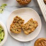 zucchini muffin split in half on a white plate.