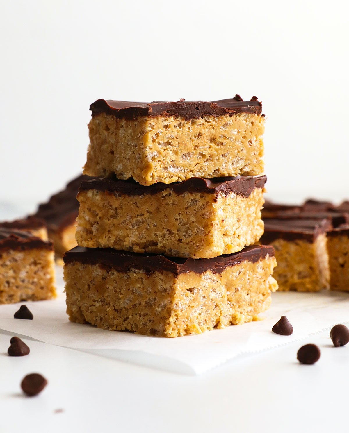 protein rice crispy treats stacked with a chocolate topping on white parchment paper.