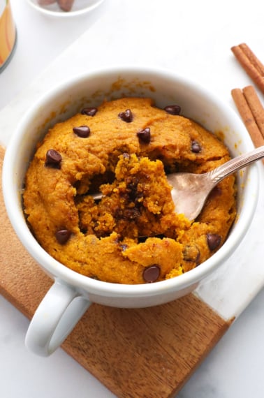 pumpkin mug cake with a fork inside the white mug.