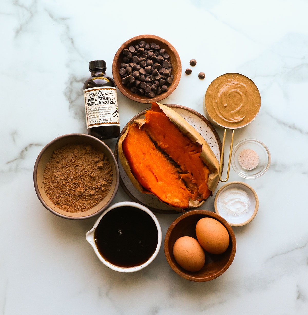 baked sweet potato, maple syrup, almond butter, eggs, vanilla extract, cacao powder, and salt in little bowls.