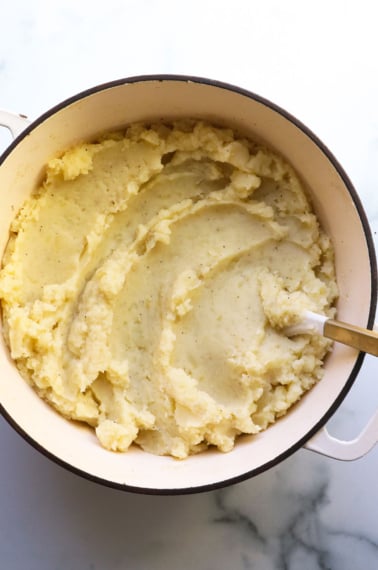 mashed potatoes in a white pot with a wooden spoon.