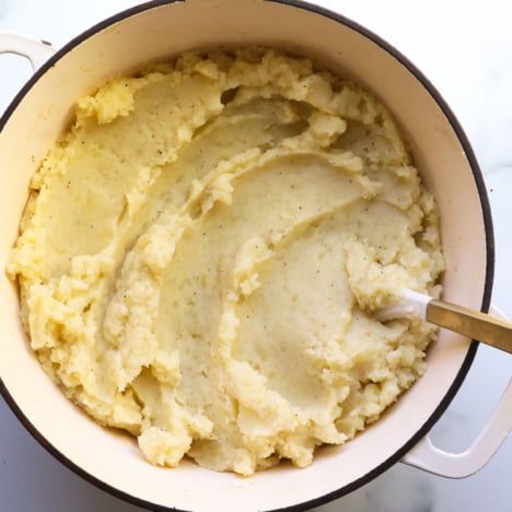 mashed potatoes in a white pot with a wooden spoon.