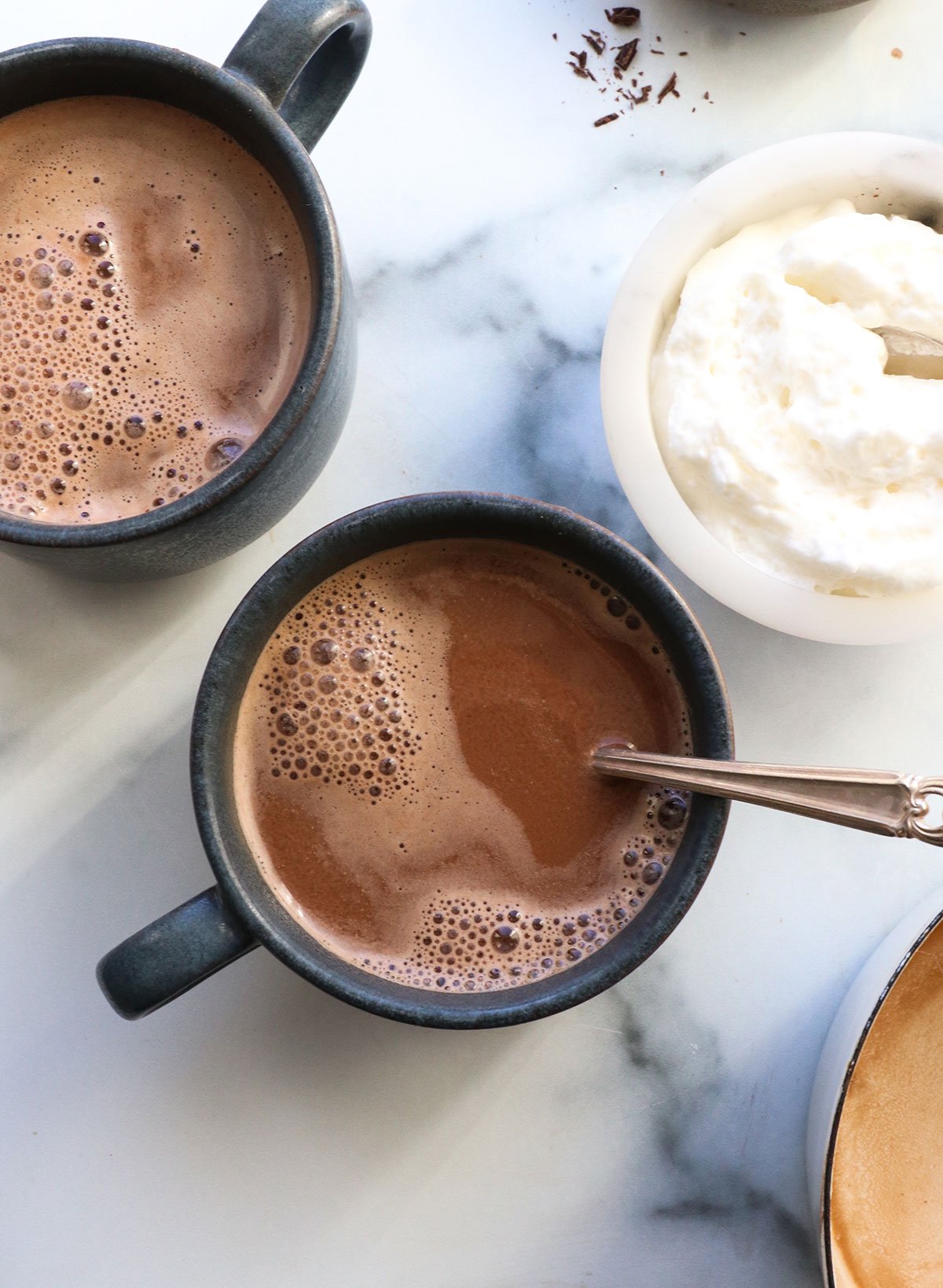 hot chocolate overhead in two blue mugs with whipped cream on the side. 