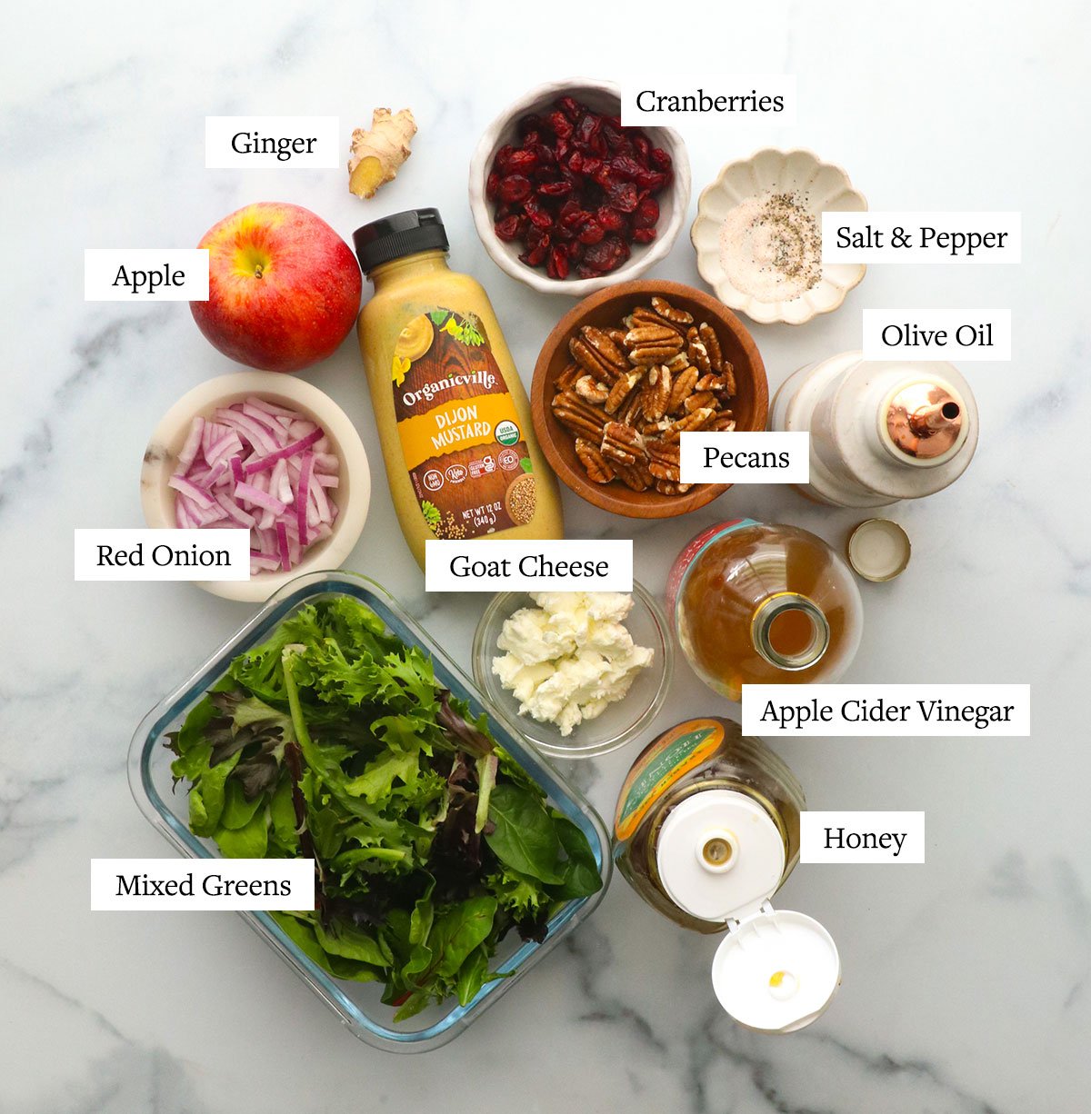 bowls of red onion, mixed greens, goat cheese, vinegar, olive oil, and honey labeled on a white surface.