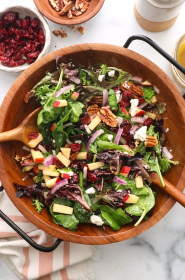 thanksgiving salad tossed with two wooden spoons near a bowl of cranberries.