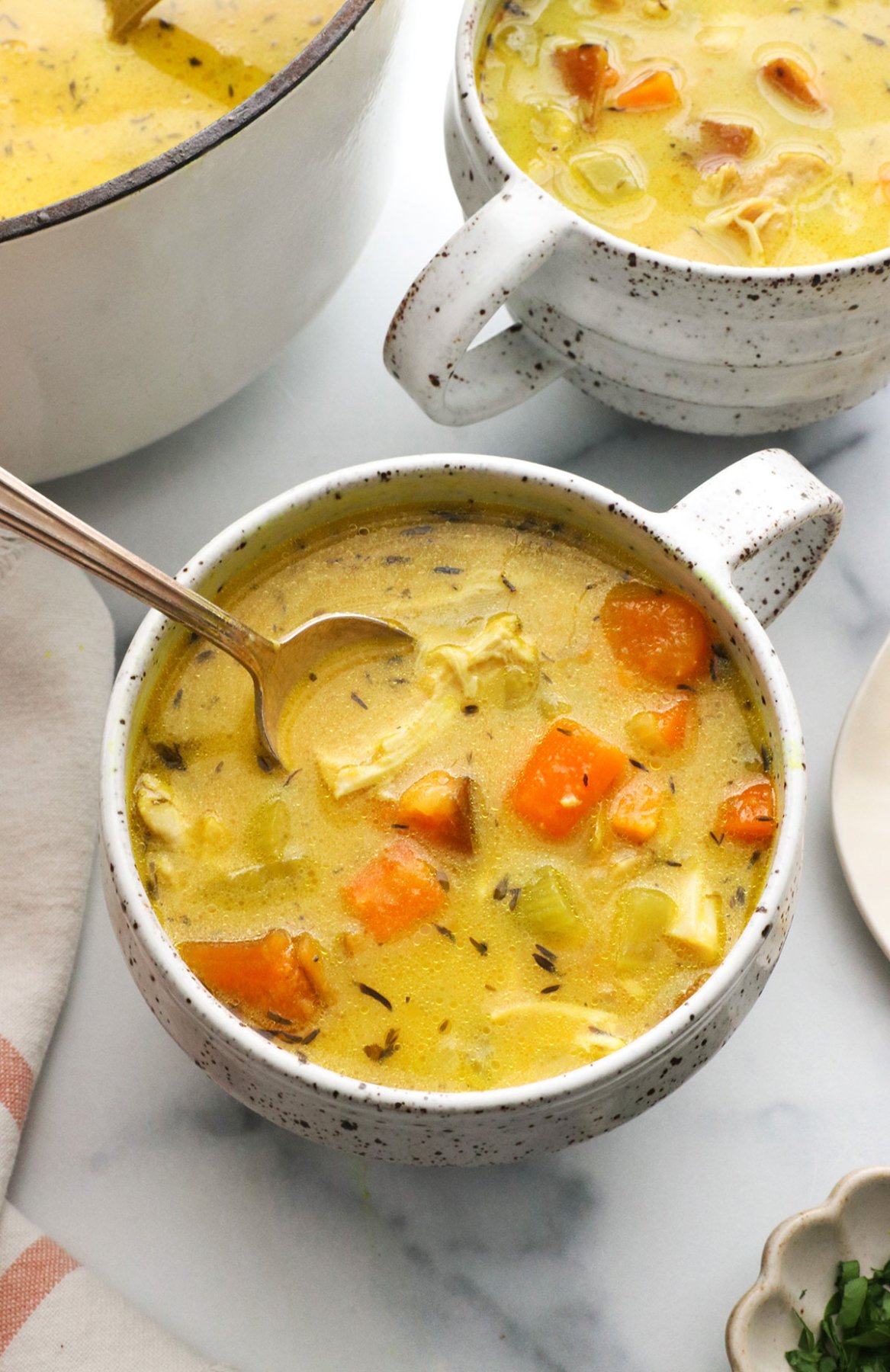 turmeric chicken soup served in white mugs with a spoon.