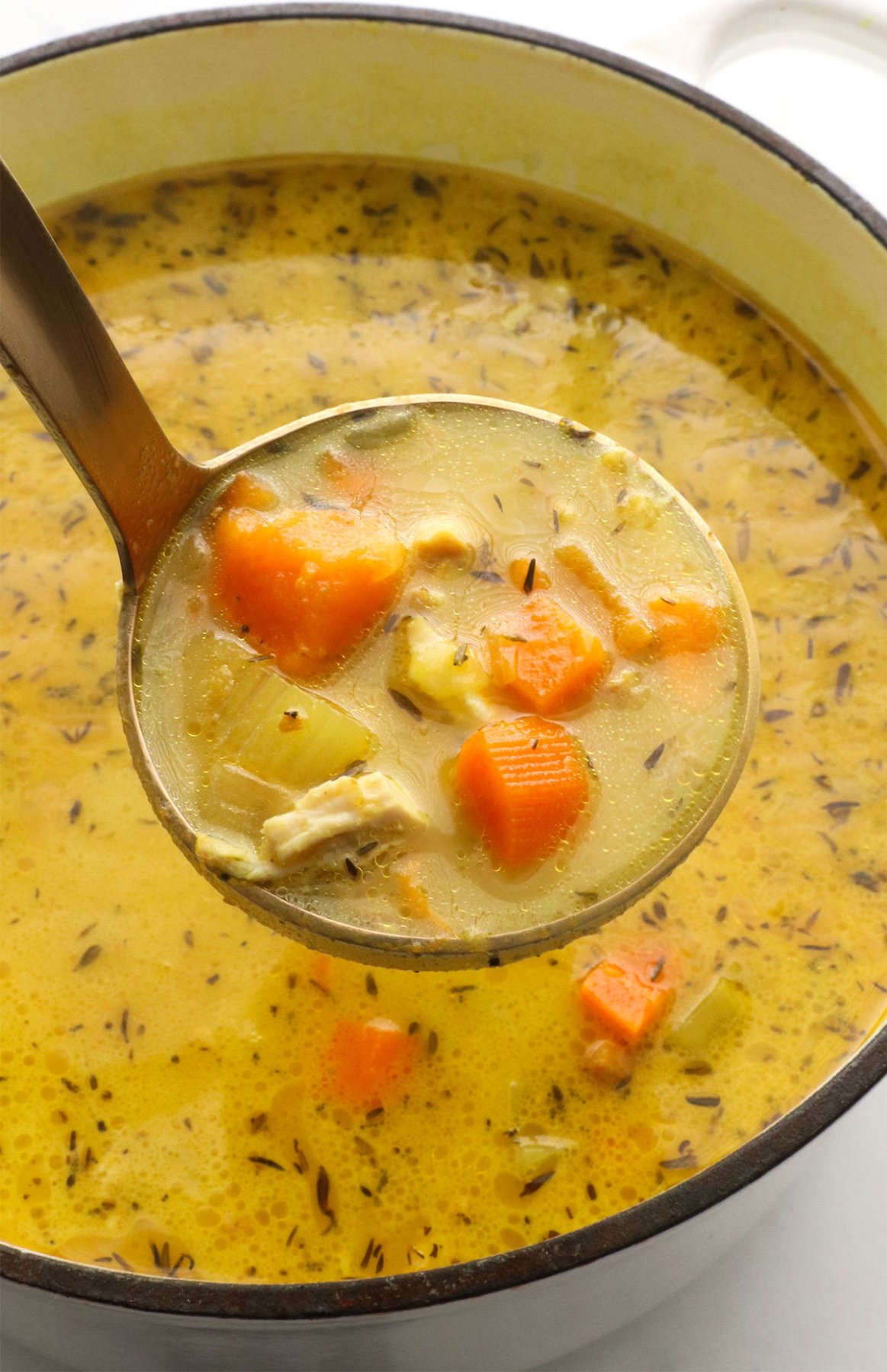 chicken turmeric soup lifted up on a ladle.