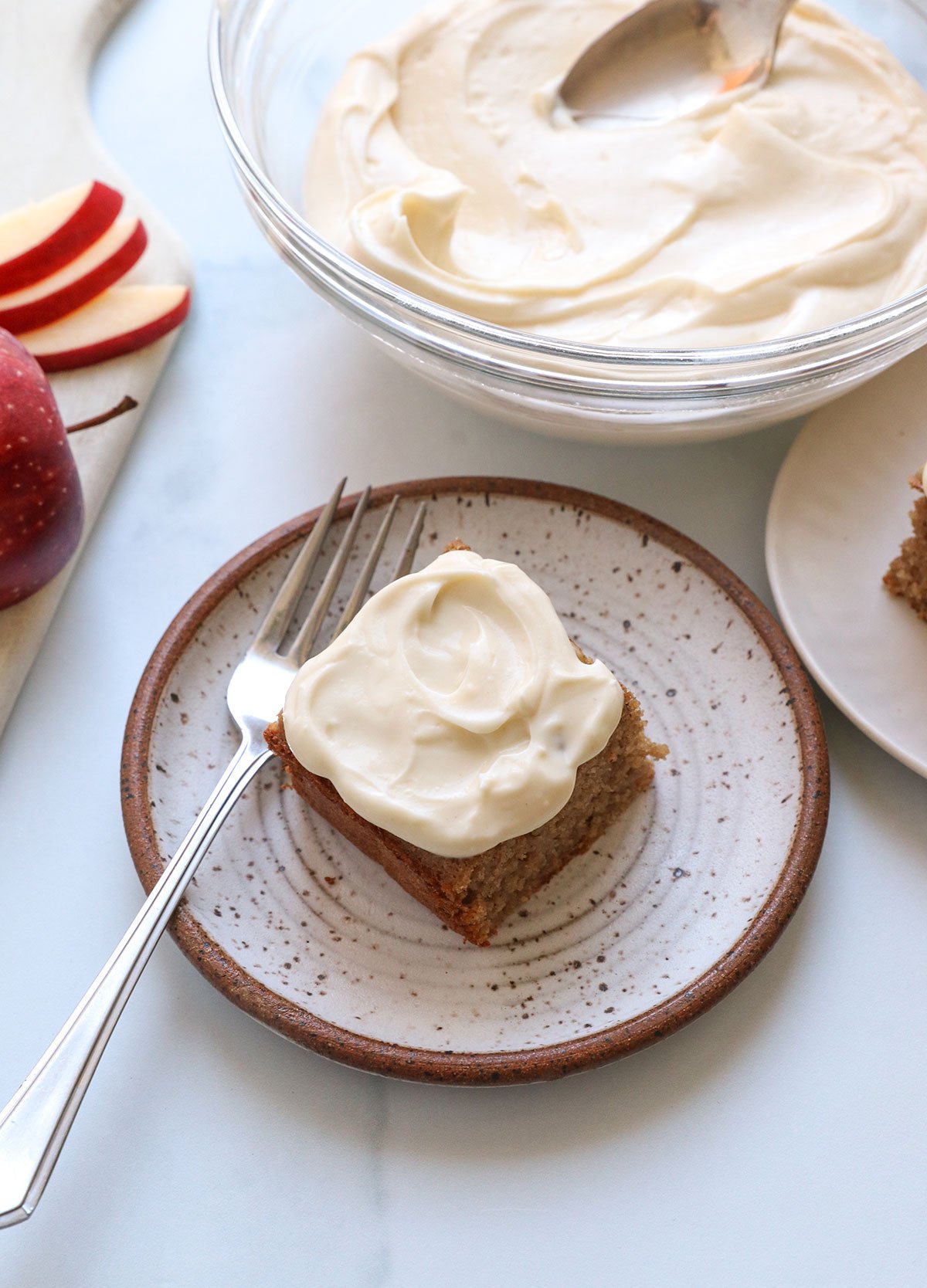 cream cheese frosting spread on top of a slice of applesauce cake on a plate.