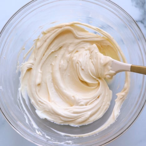 cream cheese frosting in a glass bowl stirred with a white spatula.