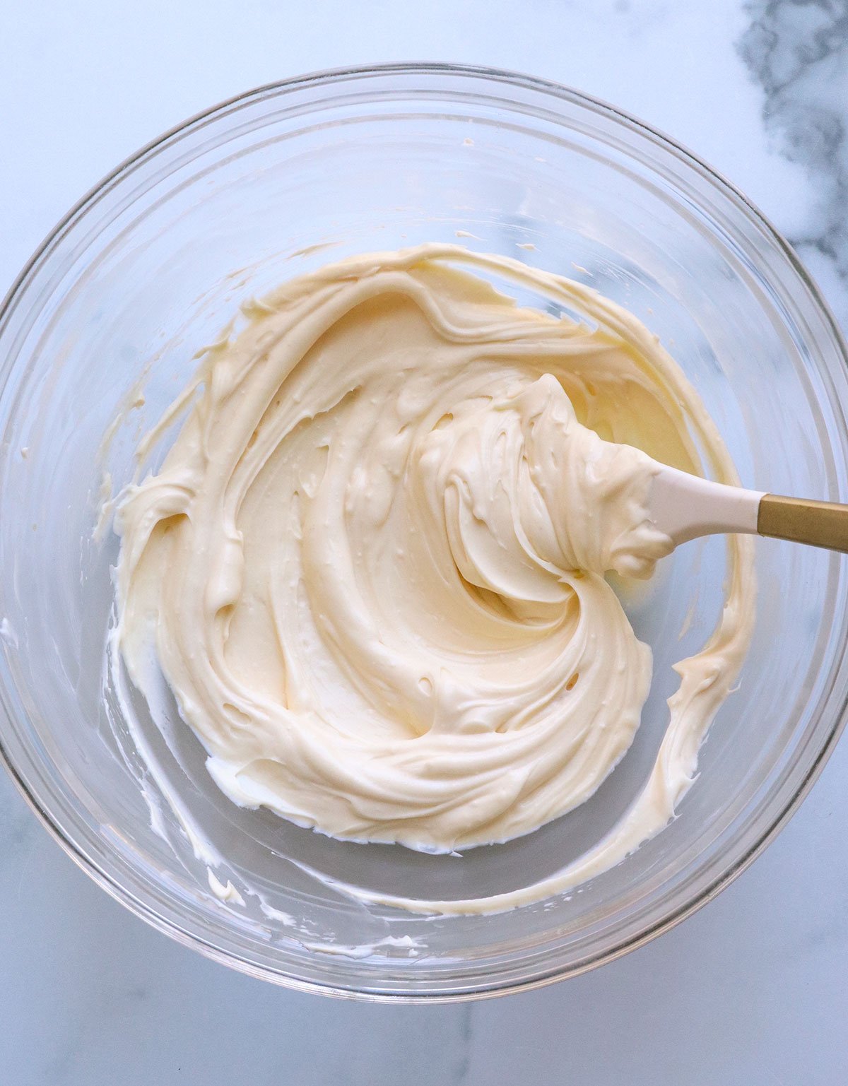 cream cheese frosting in a glass bowl stirred with a white spatula.