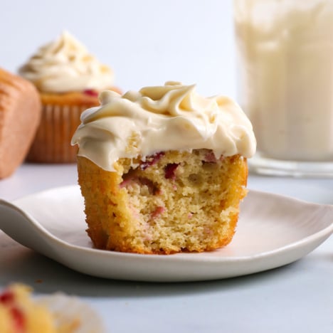 cream cheese frosting on a cranberry muffin with a bite removed.