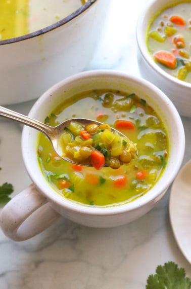 spoon lifting up some detox soup from a white mug with lentils and carrots.