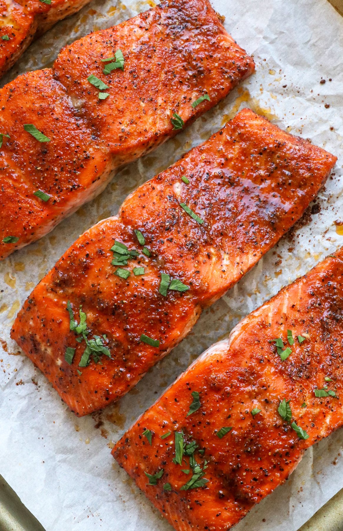 close up of baked salmon fillets on a pan with parsley on top.