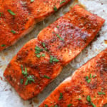 close up of baked salmon fillets on a pan with parsley on top.