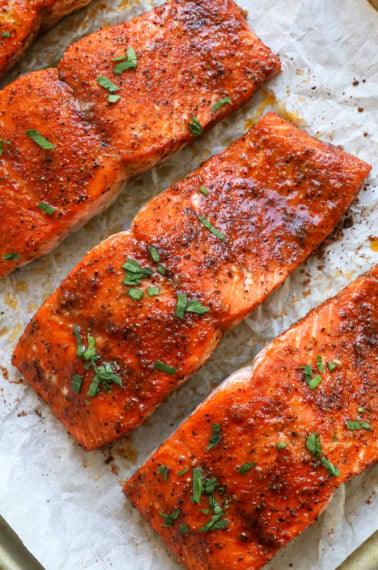 close up of baked salmon fillets on a pan with parsley on top.