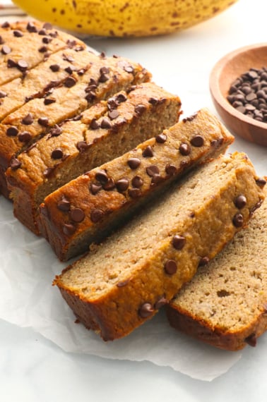 protein banana bread topped with chocolate chips and sliced on parchment paper.