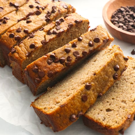 protein banana bread topped with chocolate chips and sliced on parchment paper.